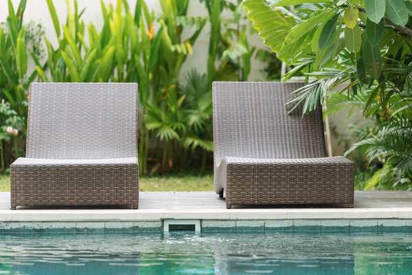 Swimming pool with brown rattan chair on poolside against natural green background standing on private territory at summer sunny day
