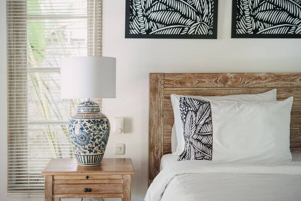 Элемент декора в белом интерьере в удобной спальне с лампой на деревянном, старом тумбочке рядом с кроватью внутри прекрасного дома
