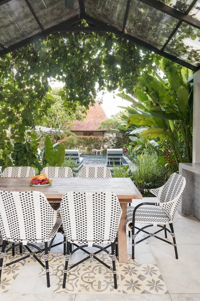 家や緑の植物を背景にしたオープンキッチンで居心地の良いダイニングルームテーブルと椅子の垂直写真 — ストック写真