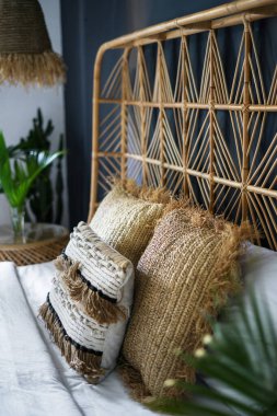 Rahat yataktaki yastıklara odaklan. Modern evdeki yatak odasının dikey fotoğrafı. Etnik dekor ve doğal yeşil bitki kompozisyonu.