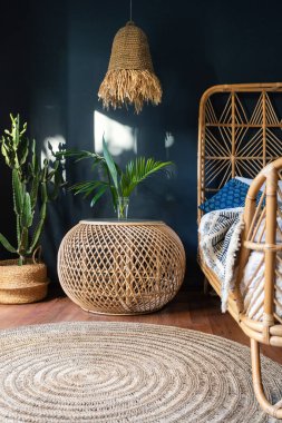 Konforlu evde iç mekan kavramı. Otantik yatak odasının etnik dekorlu dikey fotoğrafı, komodinin üzerinde lamba, yatak, hasır halı veya halı ve sepette yeşil kaktüs.