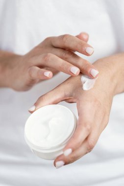Doğal kozmetik ürünlerle dolu bir konteynırı tutan genç bir kadının cildine yumuşak el kremi sürüşünün kırpılmış ve dikey görüntüsü