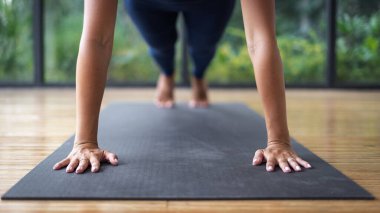 Kırpılmış görüş ve seçici odak noktası tahta pozisyonunda duran genç yetişkin atletik kadın, fitness sınıfında yoga egzersizi yapıyor, arka planda doğa ve bitkilere karşı spor giyimi eğitimi alıyor.