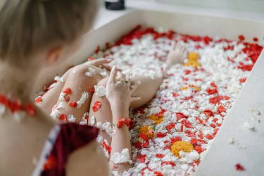 Doğal cilt bakımı kavramı. Küvette tropik çiçekli kadın bacaklarına odaklan. Genç yetişkin bir kız banyoda uzanıyor ve spa ameliyatının tadını çıkarıyor.