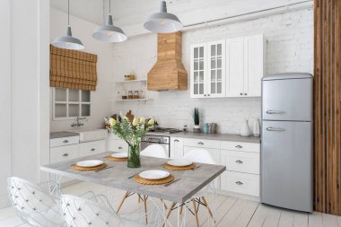 Modern mutfağın beyaz iç mekanı, yemek masası seti, gaz ocağı, buzdolabı, fırın, mobilya, ahşap dolaplar, tezgah ve pencerenin yanında lavabo.