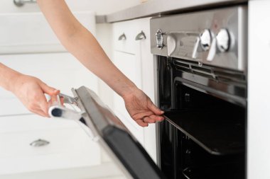 Kadının el yapımı gaz fırını ve yemek tepsisi alıp beyaz iç mekanıyla modern mutfakta durduğu görüntüler.