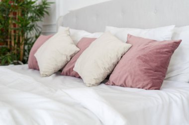 Yatak odasındaki yastıklı, battaniyeli ve beyaz fotokopi çarşaflı rahat yatağa odaklan. Işık odasındaki samimi elementler kavramı