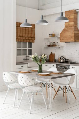 Modern iç mimari stili, mobilyası, yemek masası, gaz ocağı, fırın, ahşap dolaplar, tezgah ve pencerenin yanında lavabo olan beyaz çağdaş mutfağın dikey fotoğrafı.