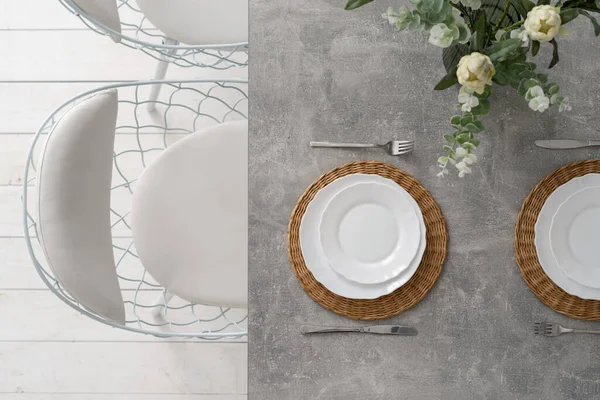 Top view of table setting at dining room with plates, cutlery, silverware and flowers in vase. Concept of fancy element in kitchen interior at modern house