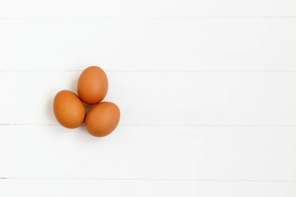 Свежие или сырые коричневые яйца на белом деревянном фоне, вид сверху, фл — стоковое фото