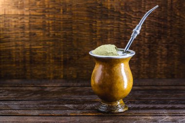 Chimarrão, or mate herb, is a South American drink left by indigenous cultures. It consists of a gourd, a pump, ground yerba mate and boiling water. Chimarrão isolated on wooden background. Copy space