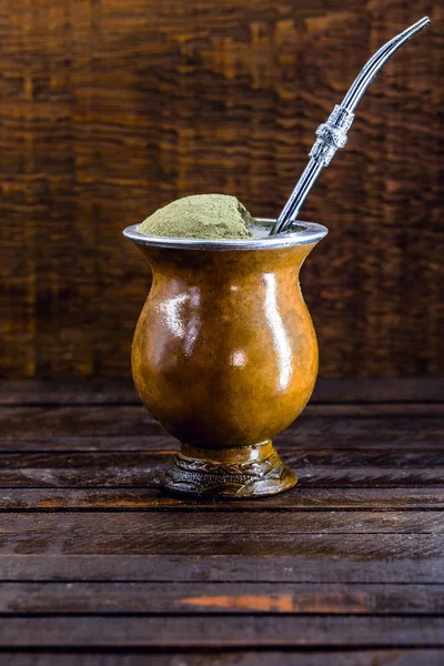 Chimarrão, or mate herb, is a South American drink left by indigenous cultures. It consists of a gourd, a pump, ground yerba mate and boiling water. Chimarrão isolated on wooden background. Copy space — Stock Fotó