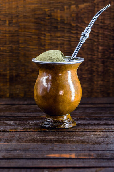 Chimarrão, or mate herb, is a South American drink left by indigenous cultures. It consists of a gourd, a pump, ground yerba mate and boiling water. Chimarrão isolated on wooden background. Copy space