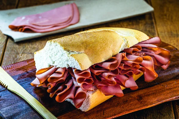 mortadella, pork slices, on italian bread, on rustic wooden background. A mortadella sandwich is any sandwich using mortadella, a large Italian sausage, and is a very popular sandwich in Brazil.
