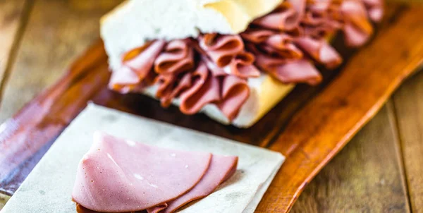 mortadella, pork slices, on italian bread, on rustic wooden background. A mortadella sandwich is any sandwich using mortadella, a large Italian sausage, and is a very popular sandwich in Brazil.