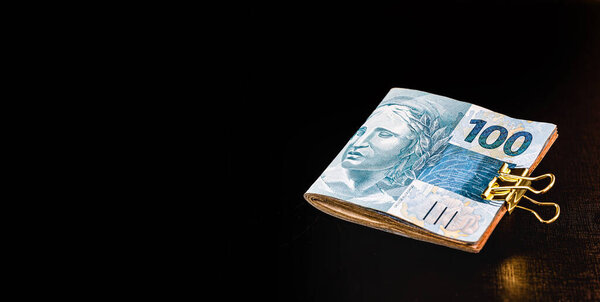 банкноты в сто реалов и пятьдесят реалов, с монетами одного реального, деньги из Бразилии. Изолированный на черном фоне. Концепция финансового кризиса и краха фондового рынка
.