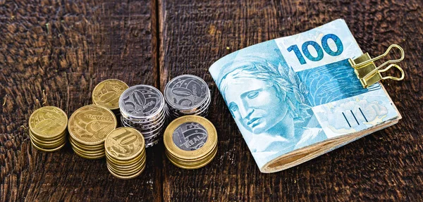 money and banknotes of 100 reais from brazil, coins from one real on a well lit rustic wooden background. Personal finance and private savings, capitalization and personal investments.