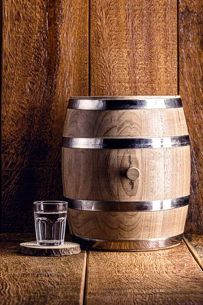 Old oak barrel and glass of high quality distilled alcohol. Brazilian silver cachaca, called pinga, vodka, white rum, liqueur, pure drink, Poitn, sake, brandy or Absinthe.