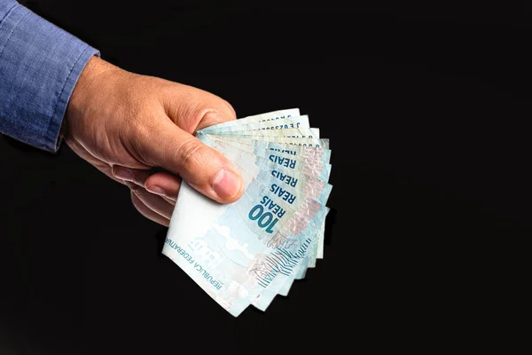 hand holding several hundred reais bills from Brazil, on isolated black background. Emergency government aid paid to microentrepreneurs, worth 600 reais
