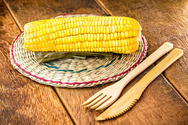 boiled corn cob, on a rustic wooden table, with recycled wood graphs, bamboo forks.