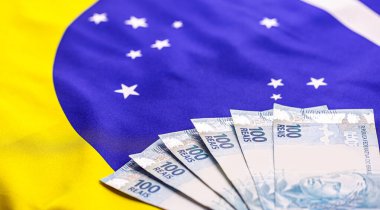 600 Brezilya reaisi, 100 reais banknotla birlikte, arkasında Brezilya bayrağı var. Brezilya 'daki ekonomik krizin imajı.