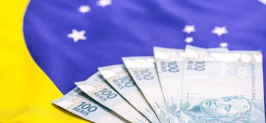 600 Brezilya reaisi, 100 reais banknotla birlikte, arkasında Brezilya bayrağı var. Brezilya 'daki ekonomik krizin imajı.