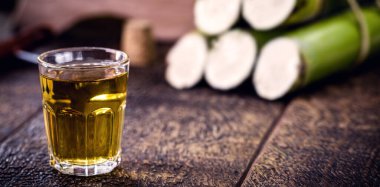Bir bardak yüksek kaliteli damıtılmış alkol. Arka planda şeker kamışı parçaları var. Brezilya cachaca 'sı (pinga denir), damla, Brezilya' dan altın rom.
