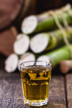 Bir bardak yüksek kaliteli damıtılmış alkol. Arka planda şeker kamışı parçaları var. Brezilya cachaca 'sı (pinga denir), damla, Brezilya' dan altın rom.
