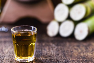 Bir bardak yüksek kaliteli damıtılmış alkol. Arka planda şeker kamışı parçaları var. Brezilya cachaca 'sı (pinga denir), damla, Brezilya' dan altın rom.