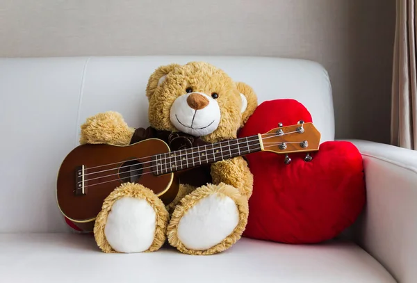 Piękny niedźwiedź ofiara lalka grając ukulele czerwone serca na sof — Zdjęcie stockowe