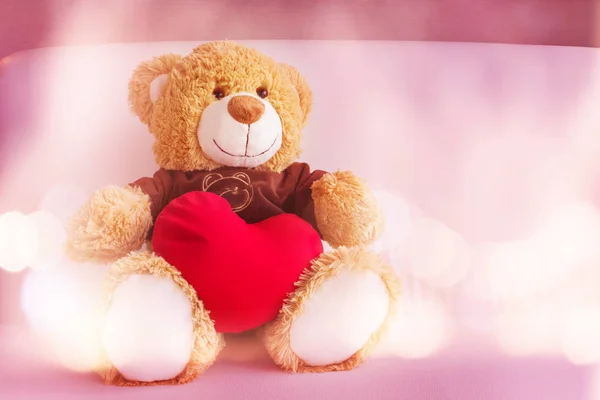 Cute bear doll with red heart smiling and sit on sofa in soft pi