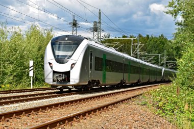 A modern electric regional train runs on a multi-lane track through natural surroundings  clipart