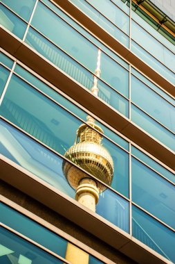 Berlin televizyon kulesi modern bir binanın cam cephesine yansıyor.
