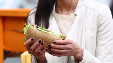 Genç kadın açık havada kafede sandviç yeme. Güzel kadın cafede sandviç yeme. Çekici kadın parkta, bir sandviç yeme müzik