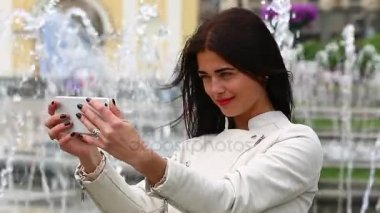 Smartphone kullanarak gülen kız portresi. Cep telefonu çeşme arka plan üzerinde olan genç ve güzel kadın. Şehir Parkı, atış Steadicam Smartphone kullanan oldukça mutlu kadın.