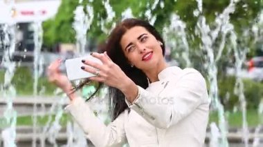 Smartphone kullanarak gülen kız portresi. Cep telefonu çeşme arka plan üzerinde olan genç ve güzel kadın. Şehir Parkı, atış Steadicam Smartphone kullanan oldukça mutlu kadın.