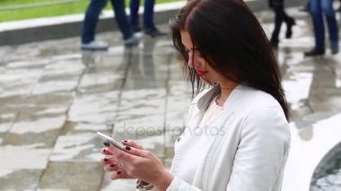 Smartphone kullanarak gülen kız portresi. Cep telefonu çeşme arka plan üzerinde olan genç ve güzel kadın. Şehir Parkı, atış Steadicam Smartphone kullanan oldukça mutlu kadın.