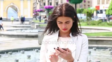Smartphone kullanarak gülen kız portresi. Cep telefonu çeşme arka plan üzerinde olan genç ve güzel kadın. Şehir Parkı, atış Steadicam Smartphone kullanan oldukça mutlu kadın.