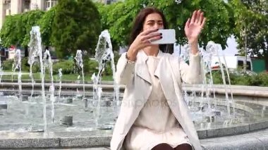 Smartphone kullanarak gülen kız portresi. Cep telefonu çeşme arka plan üzerinde olan genç ve güzel kadın. Şehir Parkı, atış Steadicam Smartphone kullanan oldukça mutlu kadın.
