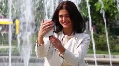 Çeşme arka plan üzerinde cep telefonu ile genç ve güzel kadın.