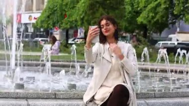 Çeşme arka plan üzerinde cep telefonu ile genç ve güzel kadın.