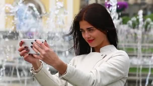 Portrait of girl laughing using smartphone. Pretty young woman with her mobile phone on fountain background. Pretty happy woman using smartphone in city park, Steadicam shot. — Stock Video