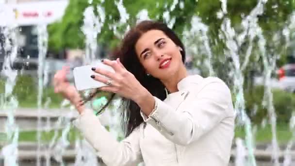 Retrato de menina rindo usando smartphone. Uma jovem bonita com o telemóvel no fundo da fonte. Mulher muito feliz usando smartphone no parque da cidade, Steadicam tiro . — Vídeo de Stock