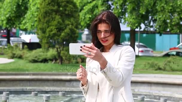 Portret van meisje lachen met behulp van de smartphone. Mooie jonge vrouw met haar mobiele telefoon op de achtergrond van de fontein. Vrij gelukkig vrouw met behulp van smartphone in stadspark, Steadicam schot. — Stockvideo