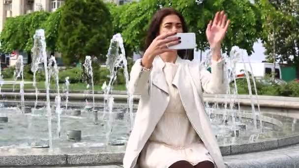 Retrato de menina rindo usando smartphone. Uma jovem bonita com o telemóvel no fundo da fonte. Mulher muito feliz usando smartphone no parque da cidade, Steadicam tiro . — Vídeo de Stock