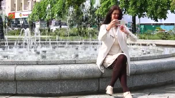 Jolie jeune femme avec son téléphone portable sur fond de fontaine . — Video