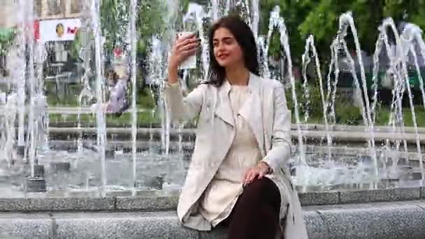 Mooie jonge vrouw met haar mobiele telefoon op de achtergrond van de fontein. — Stockvideo