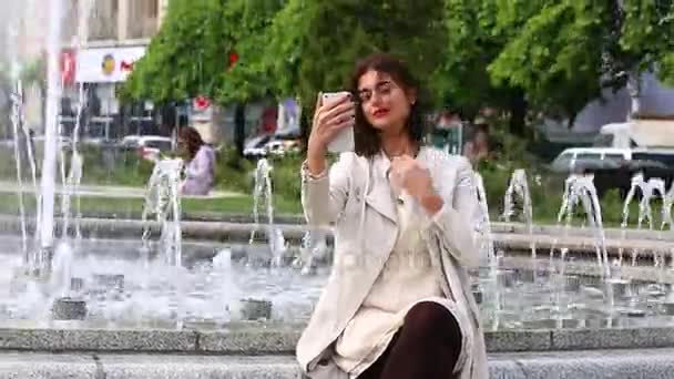 Bella giovane donna con il suo telefono cellulare su sfondo fontana . — Video Stock
