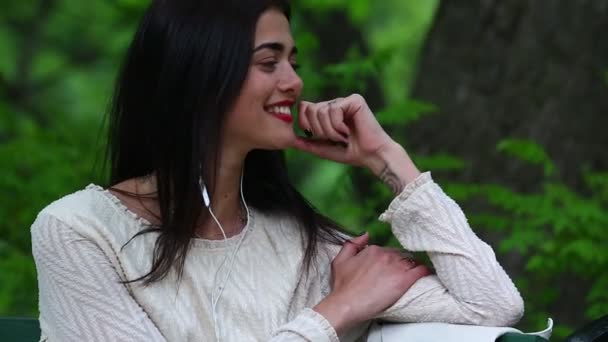 Femme écoutant la musique d'un téléphone intelligent avec écouteurs dans un parc . — Video
