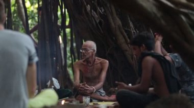 Arambol, Goa, Hindistan - Novomber 30, 2017: Hint baba ve ateş ve sigara ot yapım büyük Hint inciri ağacı altında oturan arkadaşı